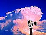 a painterly rendering of an old western windmill & dramatic storm clouds against a vivid blue sky